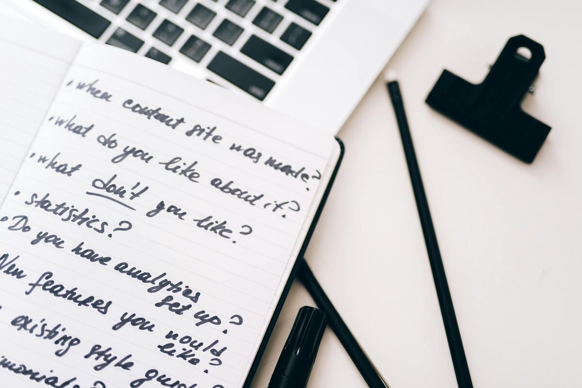 A close-up of a notebook with handwritten content ideas next to a laptop, used for content bank planning